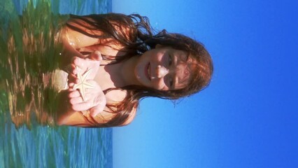 Beautiful adorable red hair child girl bathing in seawater hold starfish in hands, slow-motion. VERTICAL format