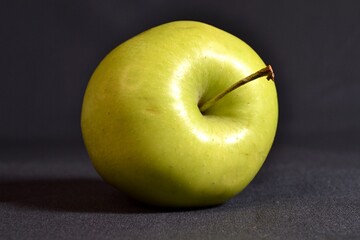 a green ripe apple in close-up on a dark background.