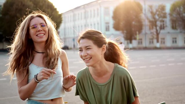Two happy young girls hug each other. Females embracing, laughing and excited. Woman friendship, walk in the city outdoors. City view, sunlight on background. Concept of love, vintage, friendship