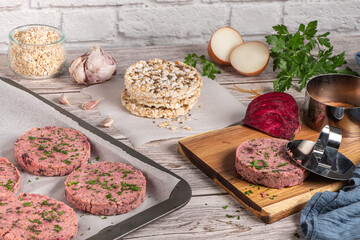 Raw veggie burger with beetroot and white beans with parsley leaves on wood cutting board.