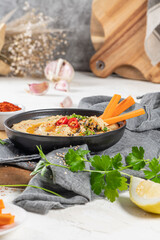 Delicious hummus in ceramic bow lwith  carrot stick dipped in hummus. Colorful snack composition on a white background.