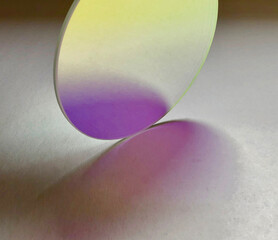 Artistic image of daylight pass through circular dichroic colour filter creating magenta pink colour shadow on white textured paper and reflection back inside the surface of the colour filter