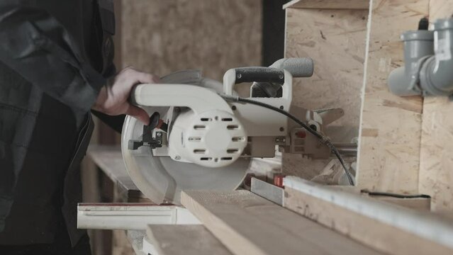 In the woodworking workshop. A worker cuts a board with a miter saw.