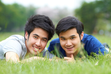 They share a love of the outdoors. Cute young gay Asian couple smiling together while lying on the...