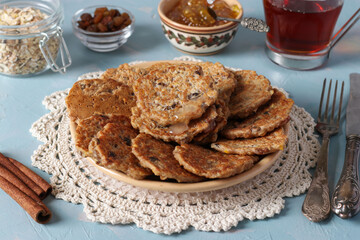 Oatmeal fritters with raisins are sprinkled with sweet syrup and served for breakfast with a cup of tea and jam