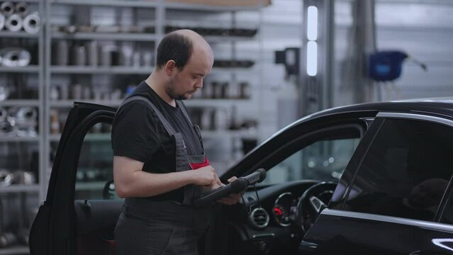 Car diagnostics. A mechanic in a close-up car service holds a tablet in his hands and presses the screen near the car