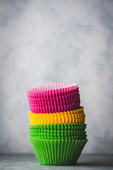 pila de moldes de papel de colores para la preparación de magdalenas o cupcakes, sobre fondo gris claro, con espacio en blanco