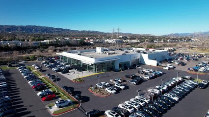 A car dealership with a full inventory in the parking lot in an suburban community - aerial flyover