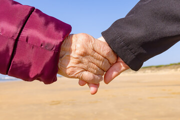 A mature woman holds her elderly mother's hand while walk by the beach