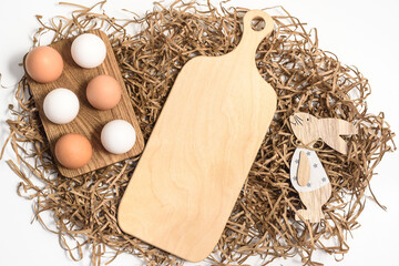 Easter mockup wood cutting board with bunny and easter eggs on wooden bowl on white background. Flat lay, top view, copyspace.