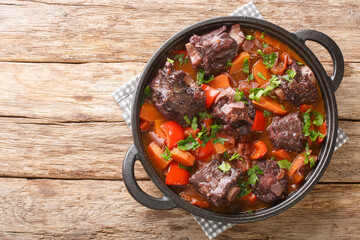 Traditional spanish dish slow cooked oxtail in red wine sauce with rabo de toro closeup on a pot on the wooden table. Horizontal top view from above - obrazy, fototapety, plakaty