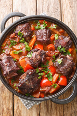 Rabo de toro or oxtail stew in cooking pot closeup on plate on the wooden table. Vertical top view from above