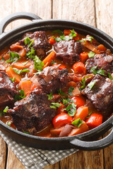 Rabo de toro or oxtail stew in cooking pot closeup on plate on the wooden table. Vertical