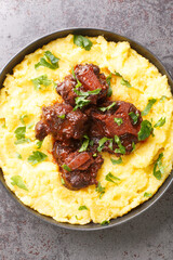 Typical dish of Brazilian cuisine Rabada Oxtail with corn porridge closeup on plate on the concrete table. Vertical top view from above