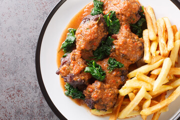 Meat for bull tail stew Rabo de toro served with french fries on white plate on the concrete table. Horizontal top view from above