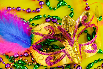 Carnival mask with feathers on yellow background. Multicolored beads Mardi Gras or Fat Tuesday...