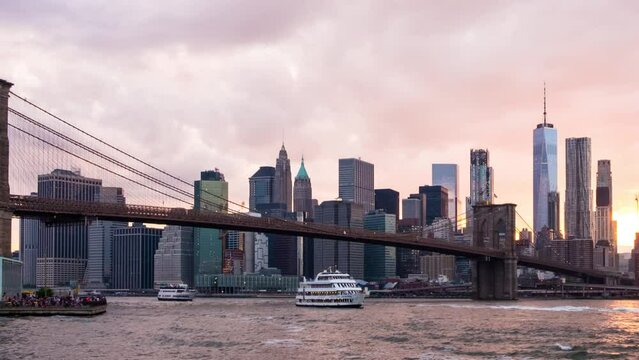 New York, USA. View of Manhattan bridge and Manhattan in New York, USA at sunset. Colorful cloudy sky with skyscrapers. Sun setting behind the skyscrapers. Time-lapse at sunset, zoom in