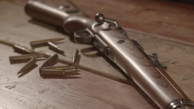 High angle dolly Live ammunition lying in front of loaded WW2 era rifle on wooden surface - close