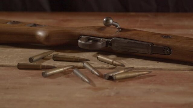 close Dolly of live ammunition lying in front of loaded WW2 era rifle on wooden surface