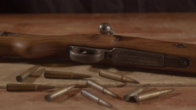 Live ammunition lying in front of loaded WW2 era rifle on wooden surface