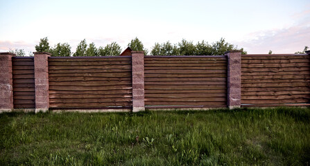 Brown wooden fence with block posts. Construction site. Corrugated surface. Private property fencing. Opaque hedge. Countryside backyard security exterior. Scandinavian, chalet or rustic style. DIY