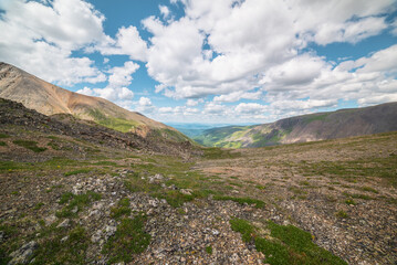 Scenic view from mountain pass to green forest valley among mountain ranges and hills on horizon at changeable weather. Green landscape with sunlit mountain vastness under cumulus clouds in blue sky.