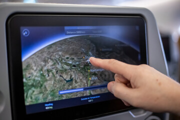 A man's hand points to an airplane on a monitor in an airplane seat. Travel and tourism.