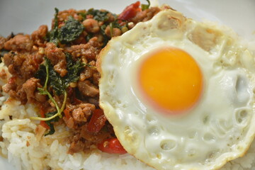 stir-fried spicy chop pork with basil leaf topping egg on rice in plate