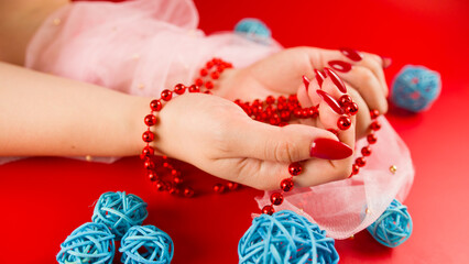 From above of crop anonymous woman with red beads and with red manicure on red background in studio with decorative wicker balls
