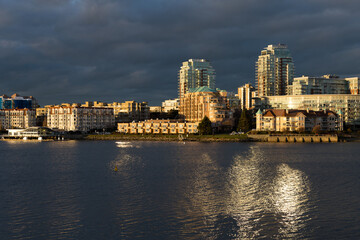 Fototapeta na wymiar The inner harbour waterfront buildings illuminated by the sun during a dramatic golden hour evening, Victoria, British Columbia, Canada