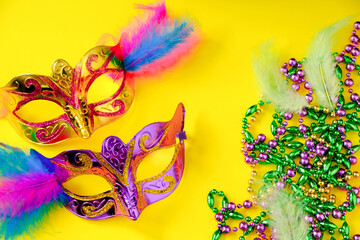 Two multi-colored carnival masks and beads on yellow background. Mardi Gras concept. Fat Tuesday...