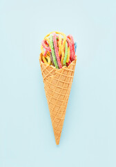 Colorful sour jelly candies in sugar sprinkles in an ice cream cone on a blue background. Flat lay, vertical.