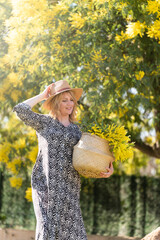 Woman with a hat in the garden walking with a mimosa tree on the background