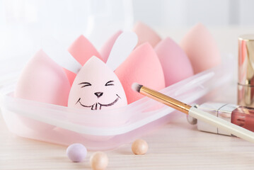Smiling rabbit with cosmetic sponges and brushes on a wooden table. Easter concept.