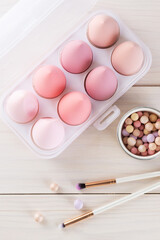 Cosmetic sponges in the form of eggs with brushes and powder on a wooden table. Vertical orientation, top view.