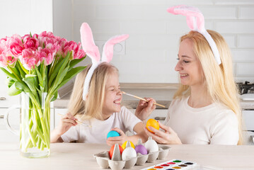 Obraz na płótnie Canvas Smiling mother and daughter with bunny ears paint Easter eggs.