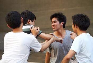 Teen rivalry. Asian teen shoving his friend while another tries to break up the fight.