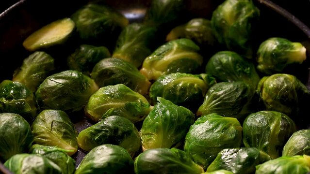 Close up shot of brussels sprouts being fried in a pan with hot steam coming out.