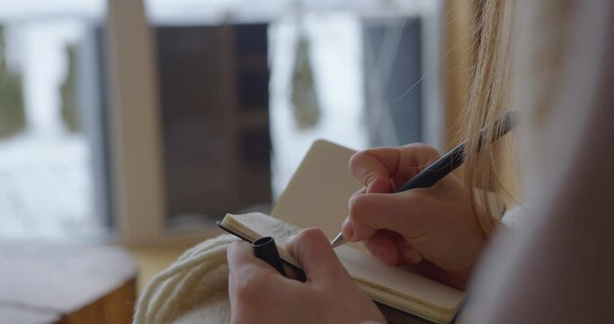 the girl writes the plan of the day in her diary diary. holds a notebook on her knees and writes thoughts in a cozy house with a wooden floor. close-up. macro