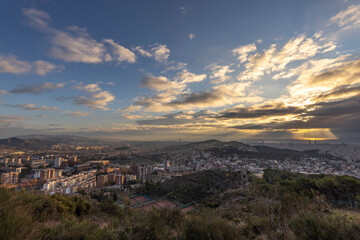 Picturesque landscape of Barcelona from the hill in the early morning. Sunbeams through the clouds. Dramatic sky over the city. Autumn in Barcelona, Spain.