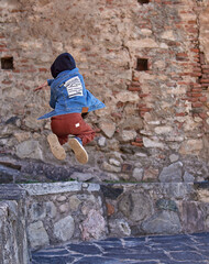 boy Child Practicing Parkour Gymnastics Outside on ancient town. kid on his back in a hooded jean...