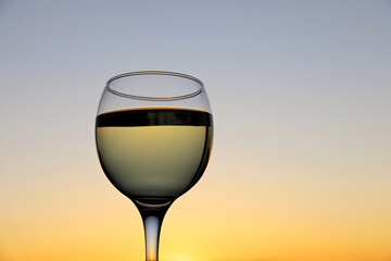 Glass with white wine on sunset sky background. Concept of celebration, evening party at resort, romantic dinner outdoors