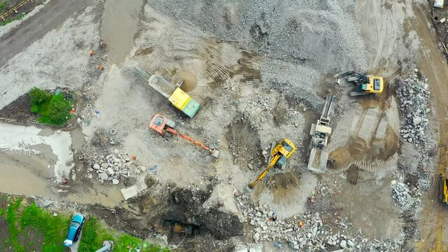 Loading cement residues into the crushing equipment and trucking soil grinding stones, aerial top view frame rotation camera. Working excavators on the site of a demolished building