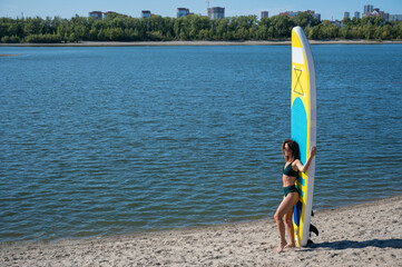 Caucasian woman walks along the beach and carries a sup board on the river in the city. Summer sport.