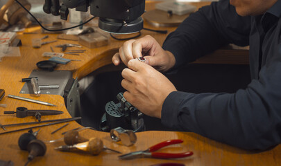 Close-up of goldsmith hand decorating precious ring with diamonds. Professional jeweler using...