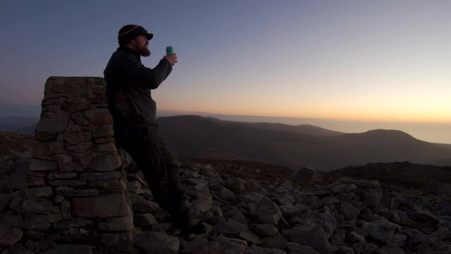 A man drinking beer on a mountain summit at sunset
