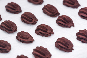 Rows of chocolate cookies on white baking paper. Image from above