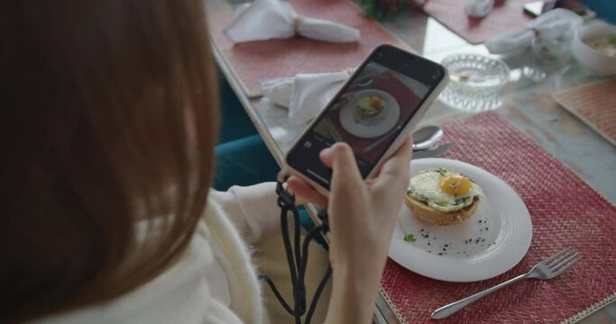 a girl at breakfast takes a picture of a sandwich with a poached egg on her phone, then takes the phone. white hands hold the phone and take off the food. dish through phone screen. close-up