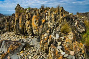 Land art with pebble trail and cairns on a with orange lichen covered rock at Cape Conran, Victoria, Australia

