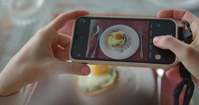 a girl at breakfast takes a picture of a sandwich sandwich with a poached egg on her phone, then takes the phone. white hands hold the phone and take off the food. dish through phone screen. macro